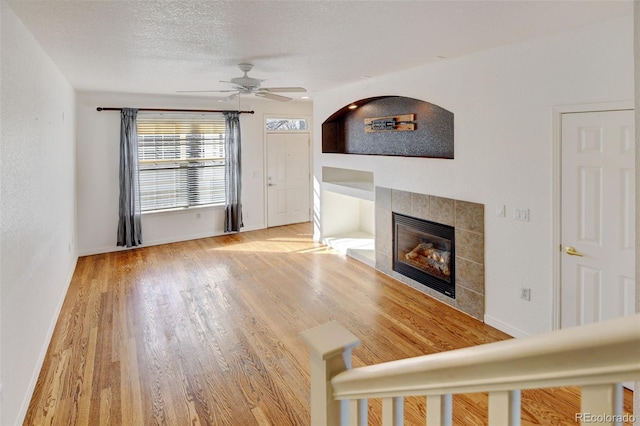 unfurnished living room featuring hardwood / wood-style flooring, ceiling fan, a tile fireplace, and a textured ceiling