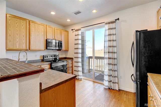 kitchen with sink, a textured ceiling, light brown cabinets, appliances with stainless steel finishes, and light hardwood / wood-style floors