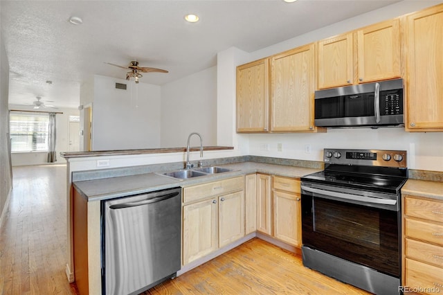 kitchen featuring appliances with stainless steel finishes, light brown cabinetry, kitchen peninsula, and sink