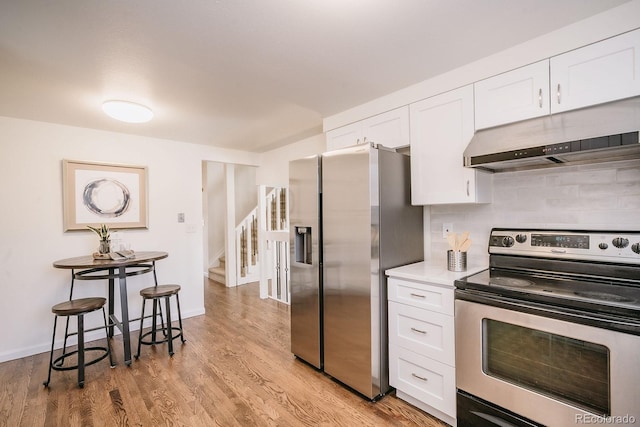 kitchen with backsplash, under cabinet range hood, light wood-style flooring, appliances with stainless steel finishes, and white cabinets