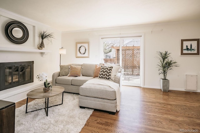 living area featuring a glass covered fireplace, crown molding, wood finished floors, and baseboards