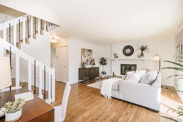 living room with a glass covered fireplace, crown molding, stairs, and wood finished floors