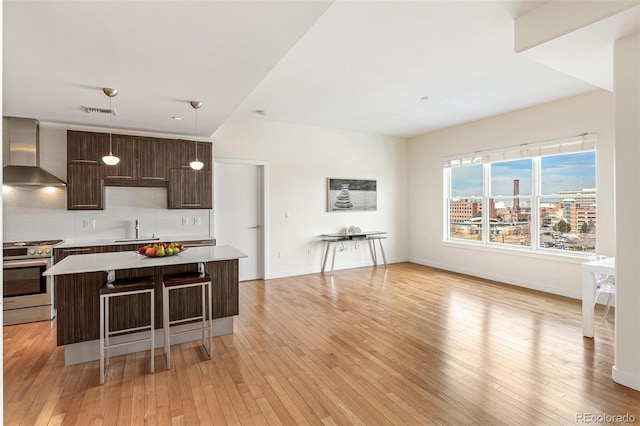 kitchen with a kitchen island, pendant lighting, dark brown cabinets, stainless steel gas range, and wall chimney exhaust hood