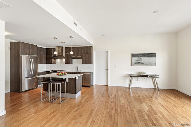 kitchen featuring wall chimney range hood, sink, stainless steel fridge, a kitchen bar, and decorative light fixtures