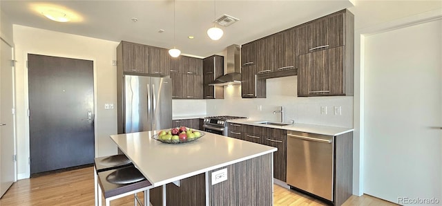 kitchen featuring wall chimney range hood, sink, a breakfast bar, appliances with stainless steel finishes, and a center island