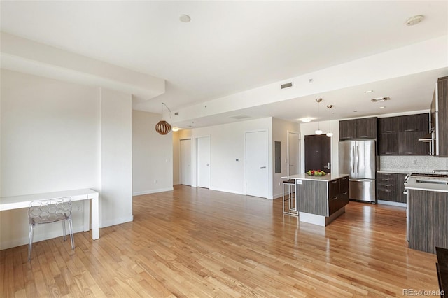 kitchen featuring stainless steel fridge, a breakfast bar area, dark brown cabinetry, a kitchen island, and decorative light fixtures