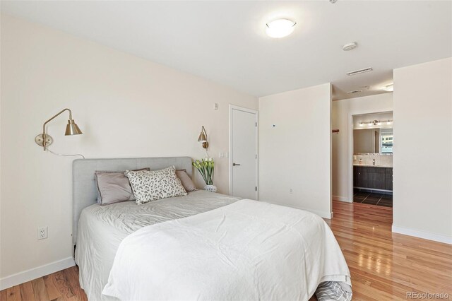 bedroom with ensuite bath and hardwood / wood-style floors