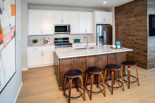 kitchen with appliances with stainless steel finishes, a kitchen island with sink, light wood-type flooring, tasteful backsplash, and sink