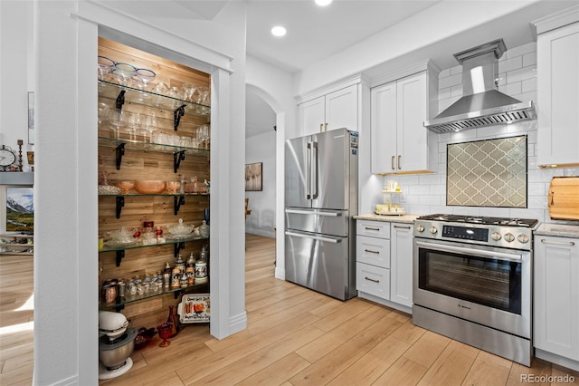 5944 S Yank Ct, Littleton, CO 80127 - kitchen with stainless steel appliances, wall chimney range hood, light wood-style flooring, arched walkways, and white cabinetry