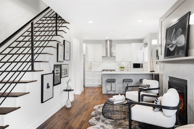 kitchen with wall chimney exhaust hood, a kitchen bar, dark wood-type flooring, white cabinetry, and decorative backsplash