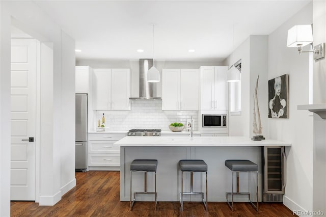 kitchen with a kitchen bar, wall chimney range hood, white cabinets, and appliances with stainless steel finishes