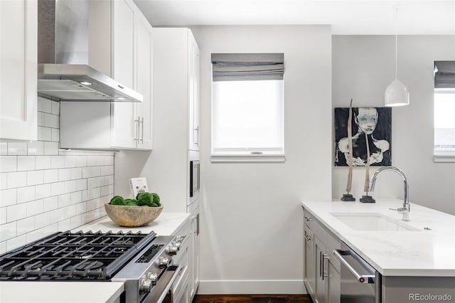 kitchen with wall chimney exhaust hood, stainless steel appliances, sink, hanging light fixtures, and light stone counters