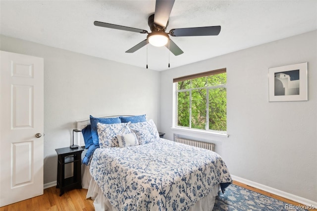 bedroom featuring radiator heating unit, light hardwood / wood-style floors, and ceiling fan