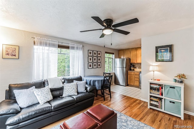 living room featuring ceiling fan, light hardwood / wood-style flooring, and a textured ceiling