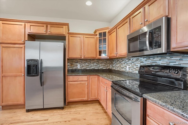 kitchen with backsplash, dark stone countertops, light hardwood / wood-style flooring, and appliances with stainless steel finishes