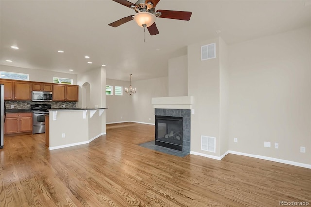 kitchen featuring ceiling fan with notable chandelier, stainless steel appliances, a fireplace, hanging light fixtures, and a breakfast bar area