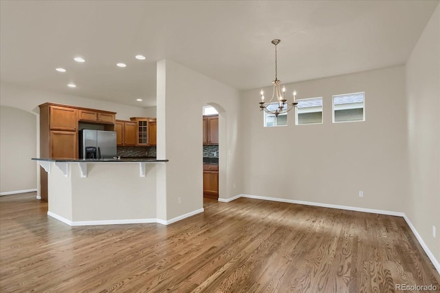 kitchen with a kitchen bar, decorative light fixtures, stainless steel refrigerator with ice dispenser, and hardwood / wood-style flooring