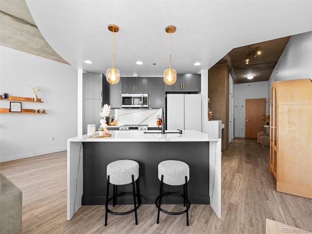 kitchen featuring light wood-style floors, stainless steel microwave, light countertops, and freestanding refrigerator