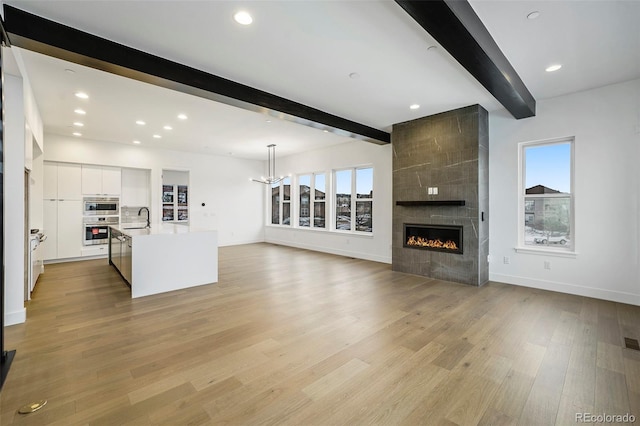 unfurnished living room featuring a healthy amount of sunlight, sink, light hardwood / wood-style flooring, and beam ceiling