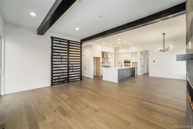 unfurnished living room featuring light wood-type flooring, a chandelier, sink, and beam ceiling