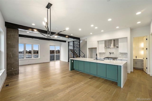 kitchen with light hardwood / wood-style floors, white cabinetry, a center island with sink, sink, and wall chimney exhaust hood