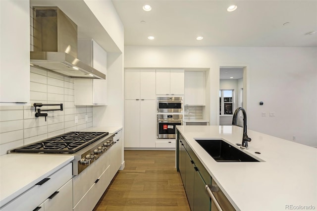 kitchen featuring stainless steel appliances, white cabinets, sink, dark hardwood / wood-style floors, and wall chimney range hood