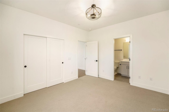 unfurnished bedroom with ensuite bathroom, light colored carpet, and a closet