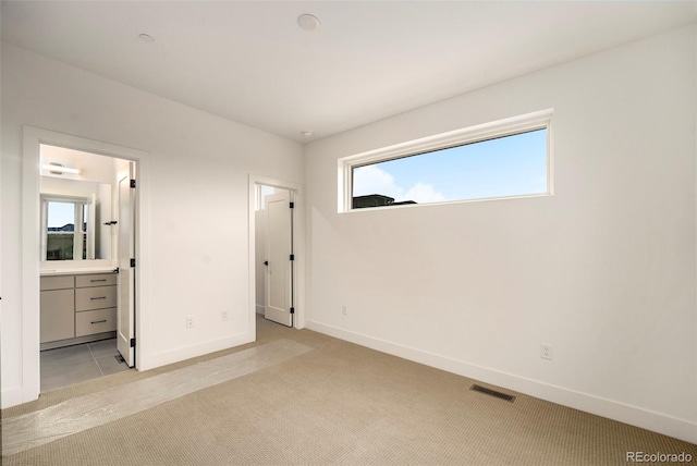 unfurnished bedroom with ensuite bath, light carpet, and multiple windows