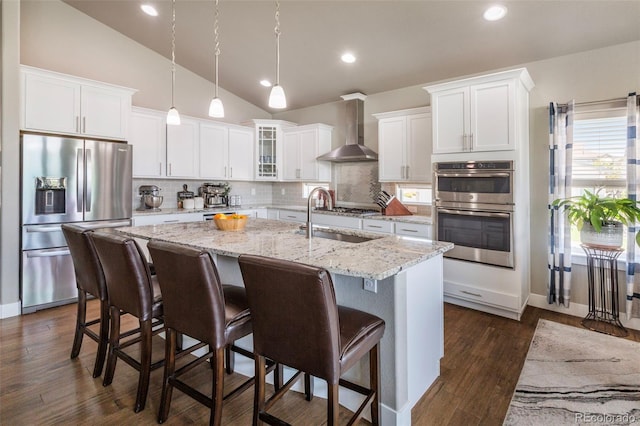 1177 Man O War Way, Colorado Springs, CO 80921 - kitchen featuring appliances with stainless steel finishes, wall chimney exhaust hood, a center island with sink, backsplash, and white cabinetry