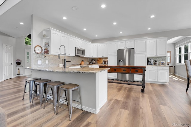 10822 Eagle Crest Ct, Parker, CO 80138 - kitchen with stainless steel appliances, open shelves, a peninsula, arched walkways, and light wood finished floors