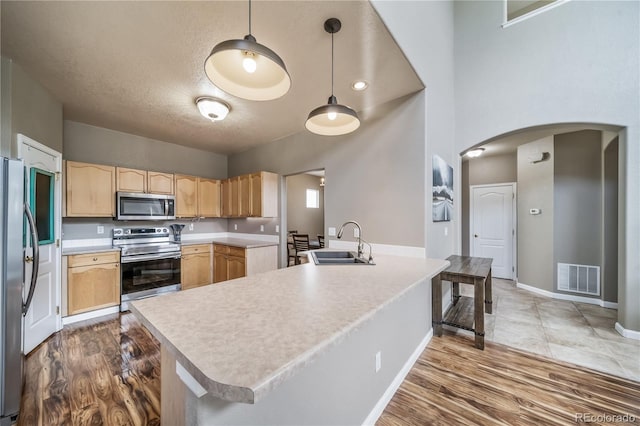 13152 E 104th Dr, Commerce City, CO 80022 - kitchen with stainless steel appliances, light brown cabinetry, arched walkways, wood finished floors, and a textured ceiling