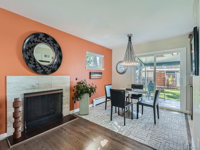 dining room with a baseboard heating unit, a tiled fireplace, and dark wood-type flooring