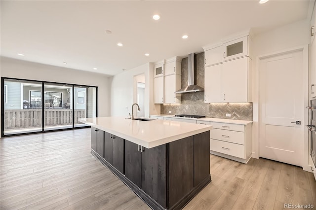 kitchen with wall chimney exhaust hood, light hardwood / wood-style floors, sink, and a kitchen island with sink