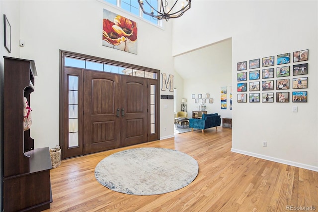 foyer entrance featuring a notable chandelier, a towering ceiling, baseboards, and wood finished floors