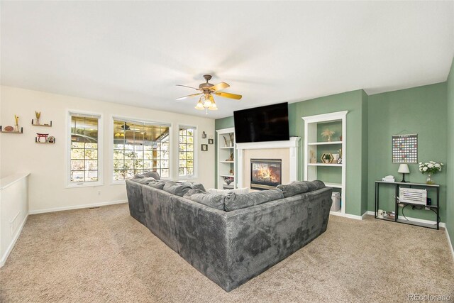 carpeted living room featuring a glass covered fireplace, a ceiling fan, and baseboards