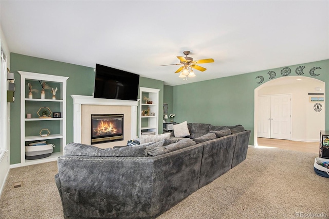 carpeted living area with ceiling fan, arched walkways, baseboards, and a glass covered fireplace