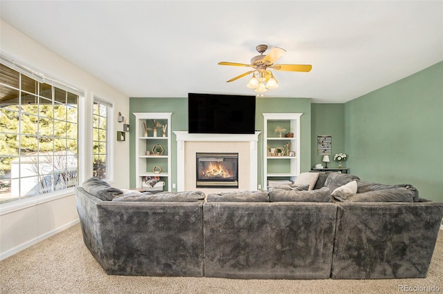 living area with baseboards, a glass covered fireplace, ceiling fan, carpet, and built in shelves