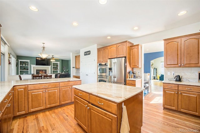 kitchen with light wood finished floors, arched walkways, stainless steel appliances, and a glass covered fireplace