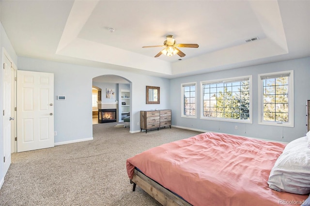 carpeted bedroom featuring a glass covered fireplace, a raised ceiling, and visible vents