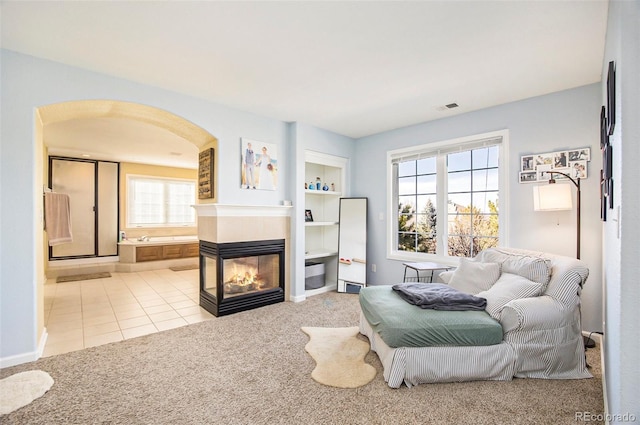 interior space with arched walkways, carpet flooring, visible vents, built in features, and a multi sided fireplace