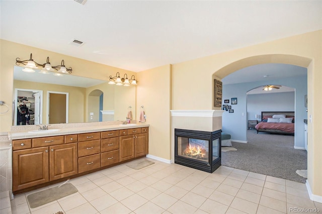 bathroom featuring double vanity, visible vents, tile patterned flooring, a sink, and a multi sided fireplace