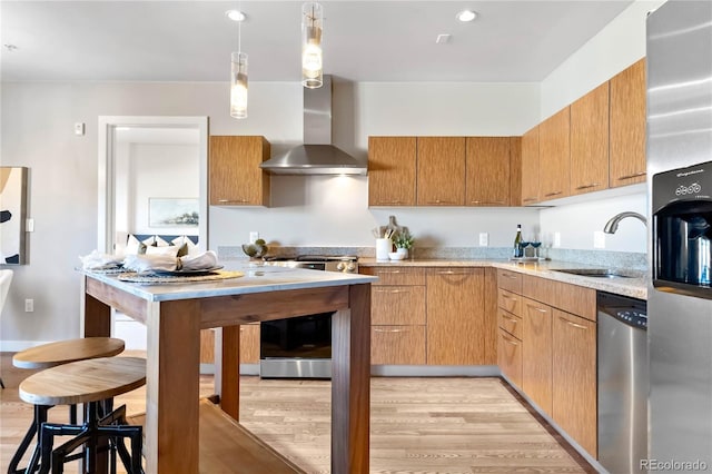 kitchen featuring wall chimney exhaust hood, sink, light wood-type flooring, appliances with stainless steel finishes, and pendant lighting