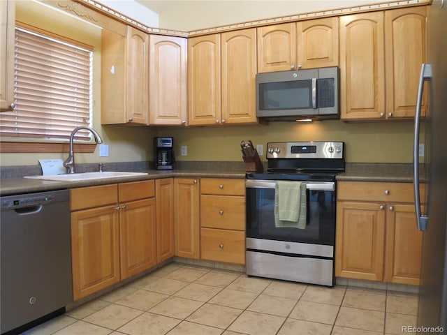 kitchen featuring light brown cabinets, dark countertops, a sink, light tile patterned floors, and stainless steel appliances