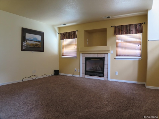unfurnished living room with baseboards, a tiled fireplace, visible vents, and carpet flooring