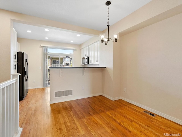 kitchen featuring hanging light fixtures, stainless steel appliances, a kitchen breakfast bar, kitchen peninsula, and white cabinets