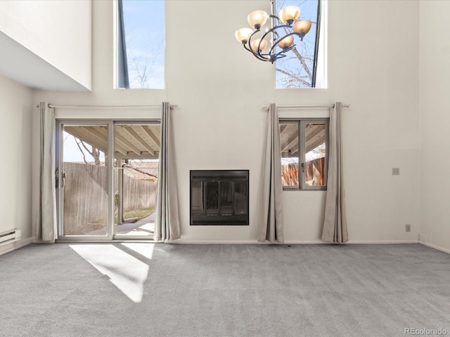 unfurnished living room with carpet, a glass covered fireplace, a towering ceiling, and an inviting chandelier