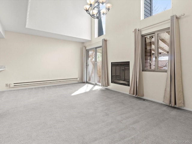 unfurnished living room with light colored carpet, a towering ceiling, baseboard heating, an inviting chandelier, and a glass covered fireplace