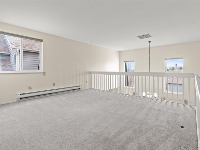 carpeted spare room featuring a healthy amount of sunlight, visible vents, and a baseboard heating unit