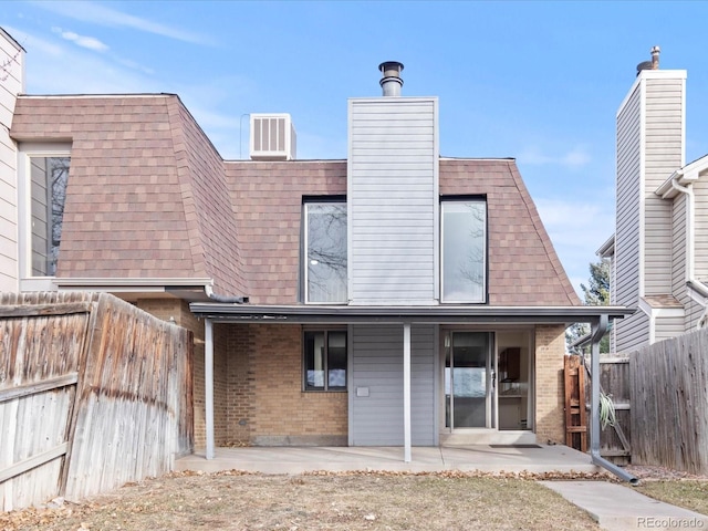 back of property with brick siding, a patio, a chimney, a shingled roof, and a fenced backyard