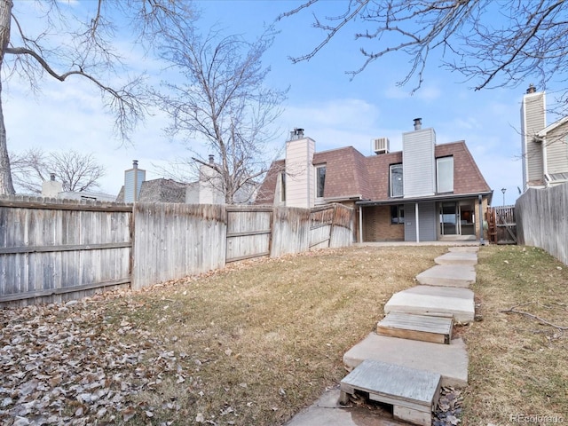 rear view of house featuring a fenced backyard, a lawn, a chimney, and brick siding